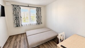 A small room with a bed, a chair, a table, and a window with curtains. - Komfortný 3 izbový byt pri centre s parkovaním (Liptovský Mikuláš)