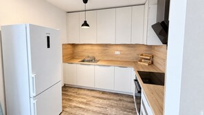 A compact kitchen with white cabinets, a wooden countertop, a built-in sink, and a black pendant light. - Komfortný 3 izbový byt pri centre s parkovaním (Liptovský Mikuláš)