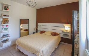 Une chambre à coucher comprenant un lit, des tables de chevet, un miroir et des étagères où sont rangés divers objets.