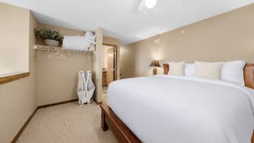A hotel room with a large bed, a ceiling fan, a hanging plant, and a coat rack.