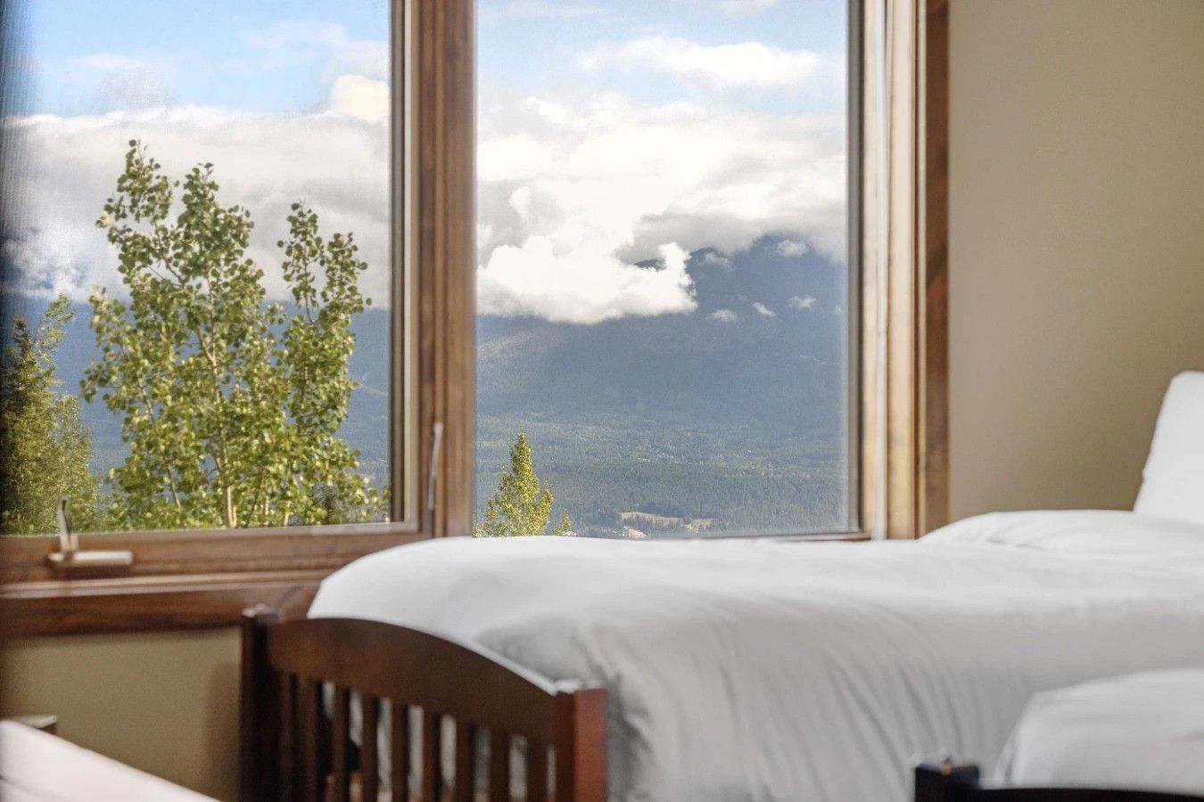 Ein Schlafzimmer mit einem Bett, einem Holzkopfende und einem Fenster mit Blick auf Bäume und Berge.