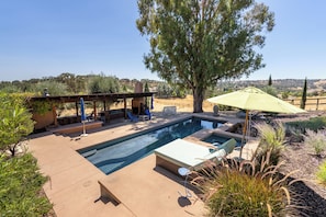 Ein Swimmingpool mit Liegestühlen und einer Pergola, umgeben von viel Grün und freiem Blick auf die Hügel.