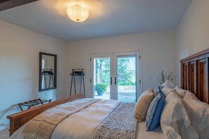 Ein Schlafzimmer mit Bett, einer Holzbank, einem Spiegel und Blick ins Freie.
