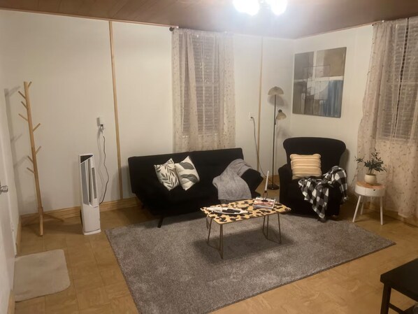 A living room with a black sofa, a leopard print coffee table, and a black armchair. There is a floor lamp and a small table with a plant.