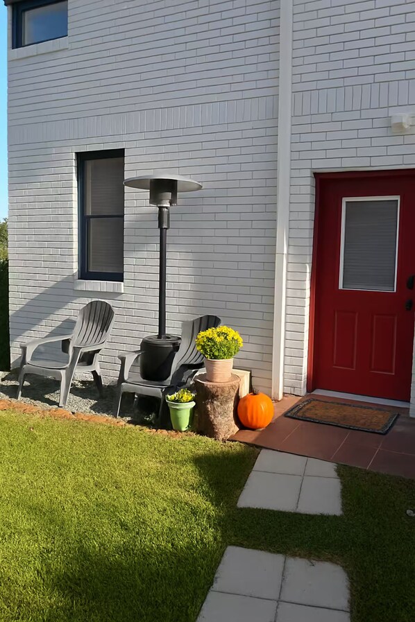A house with a red door, a white brick exterior, a lawn, a pathway, and outdoor furniture.