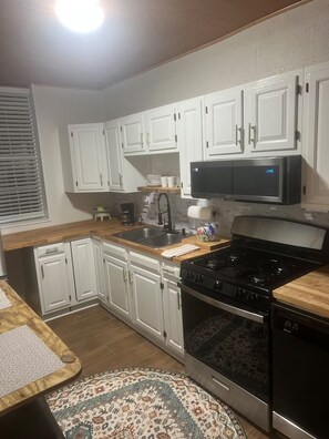A compact kitchen with white cabinets, a black stove, and a microwave.