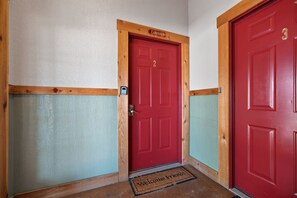 Una puerta roja con el número 2 y un marco de madera, un felpudo con la inscripción 'Welcome Friends', y una pared con textura.