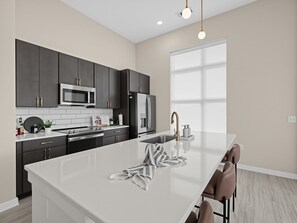 A modern kitchen with dark cabinetry, a white island, and a large window providing natural light. - Brand-new Luxury Furnished Penthouse in Noda 30 Night Mid-term Rental (Charlotte)