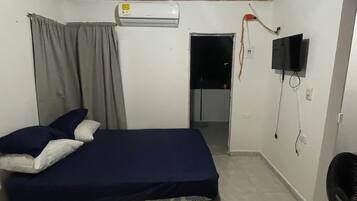 A bedroom with a bed, an air conditioner, a television, and a door leading to another room.