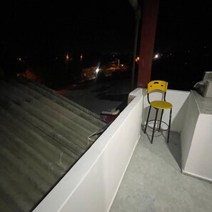 A balcony with a yellow chair, a concrete floor, and a view of a street at night. - MIRADOR MTR LODGING (Montería)