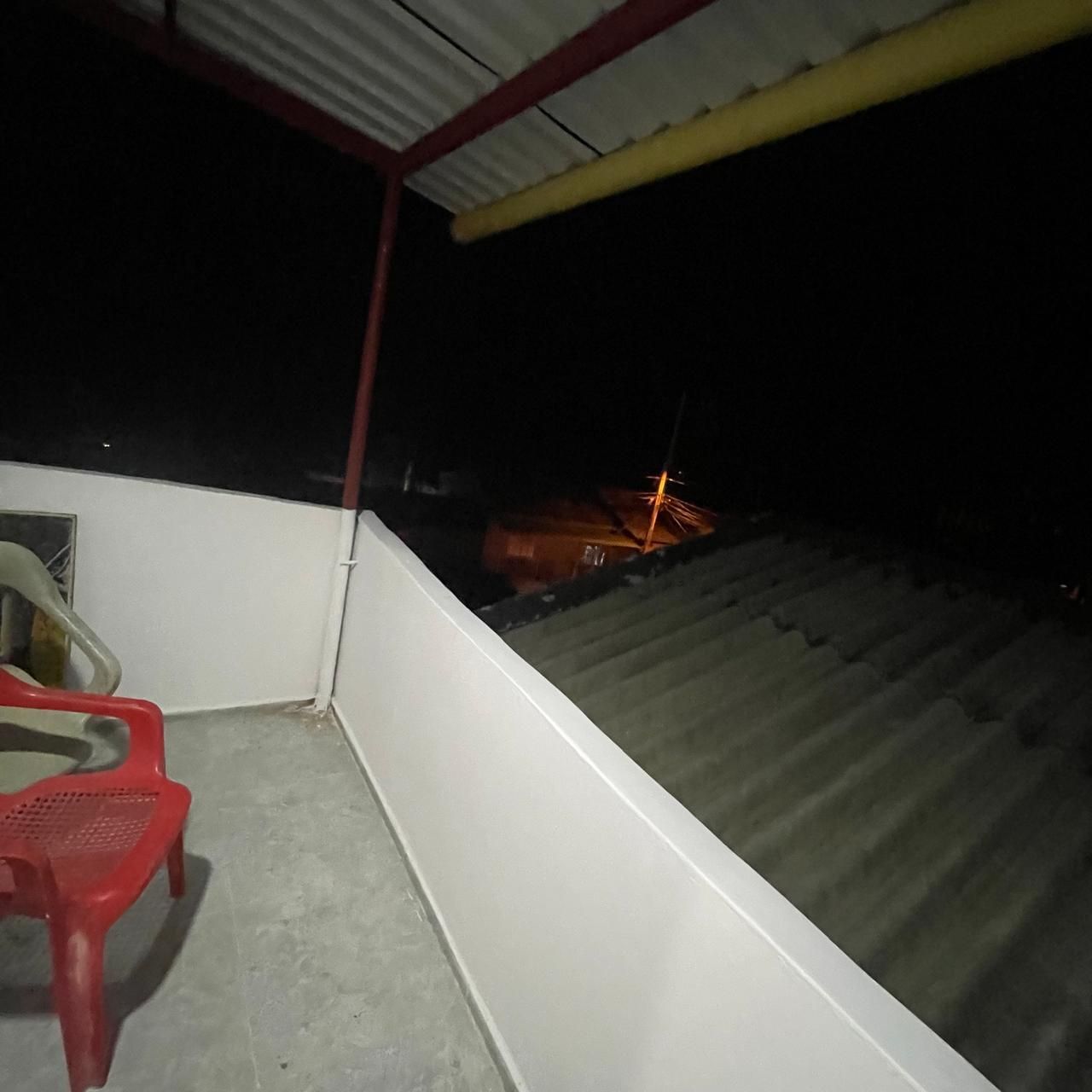 A balcony with a red plastic chair, a white wall, and a metal roof.