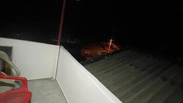 A balcony with a red plastic chair, a white wall, and a metal roof.
