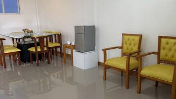 A dining area with a glass table, yellow chairs, a refrigerator, and a painting on the wall.