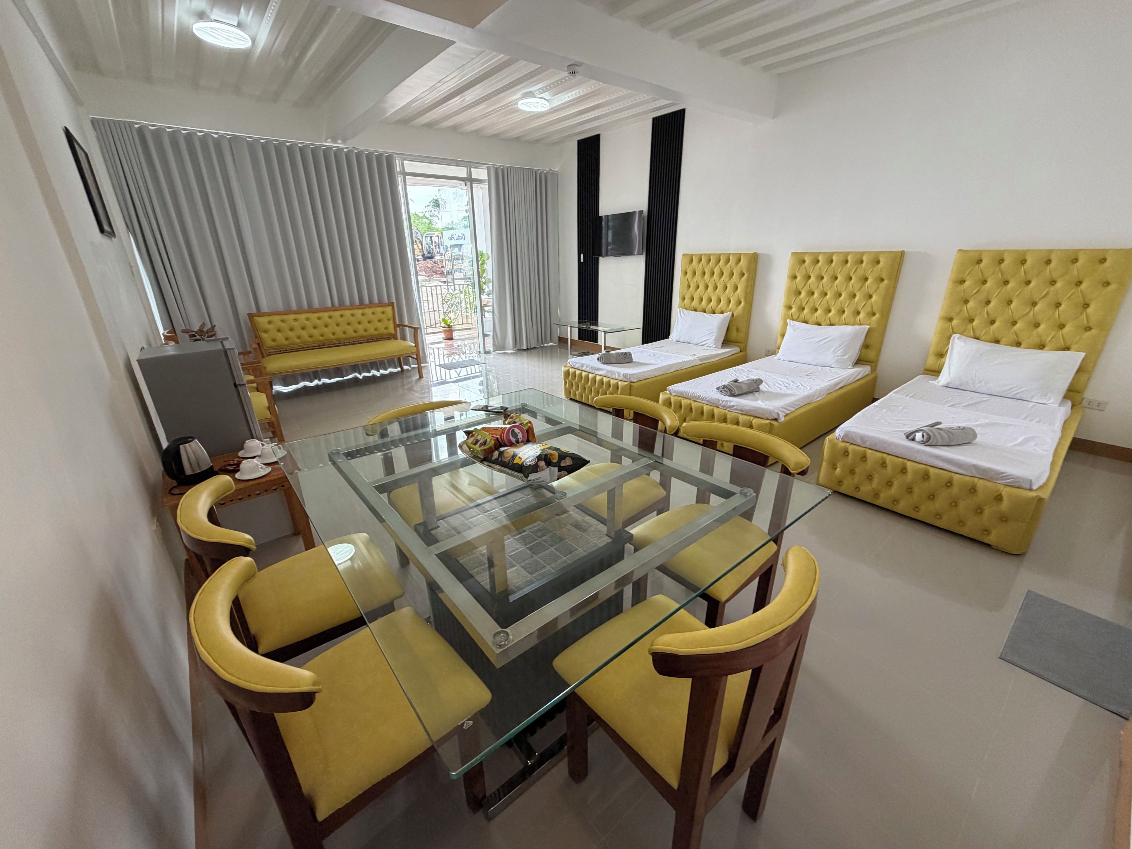 A hotel room with two beds, a glass dining table, yellow chairs, a sofa, and a TV.