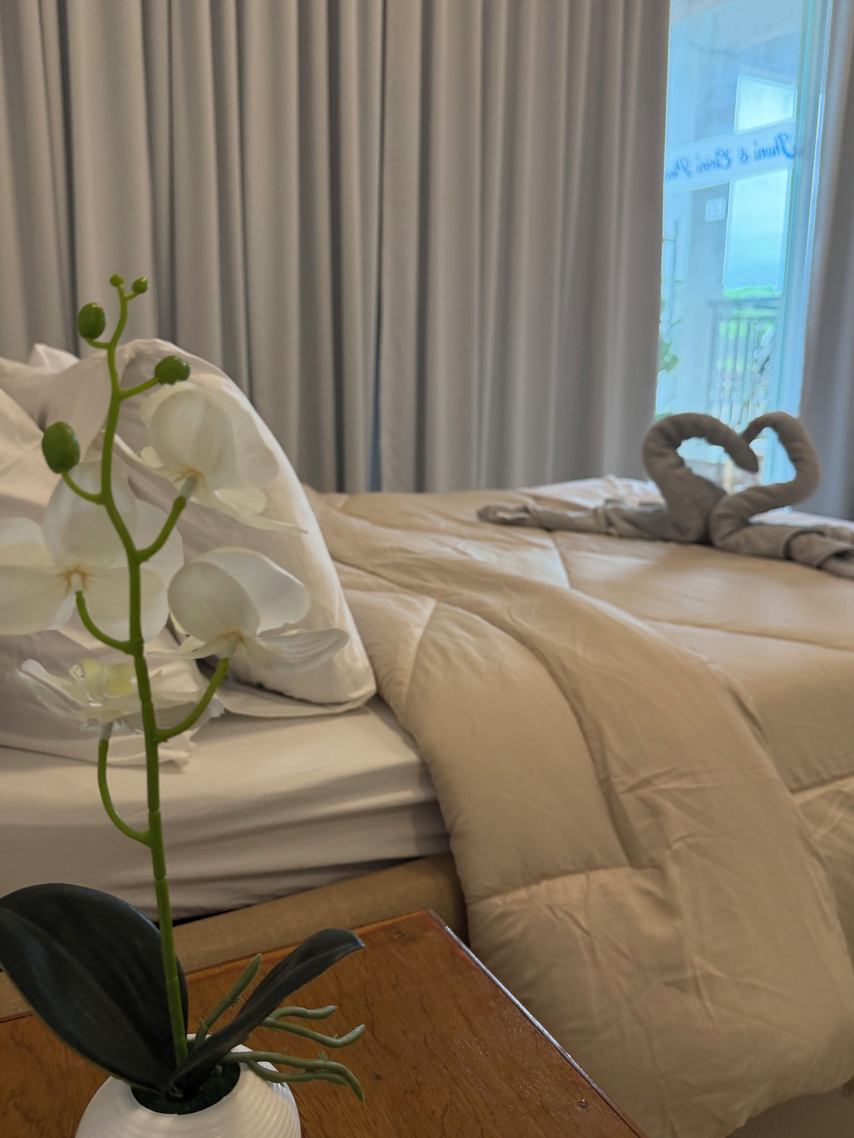 A hotel room with a bed, a heart-shaped towel arrangement, and a potted orchid.
