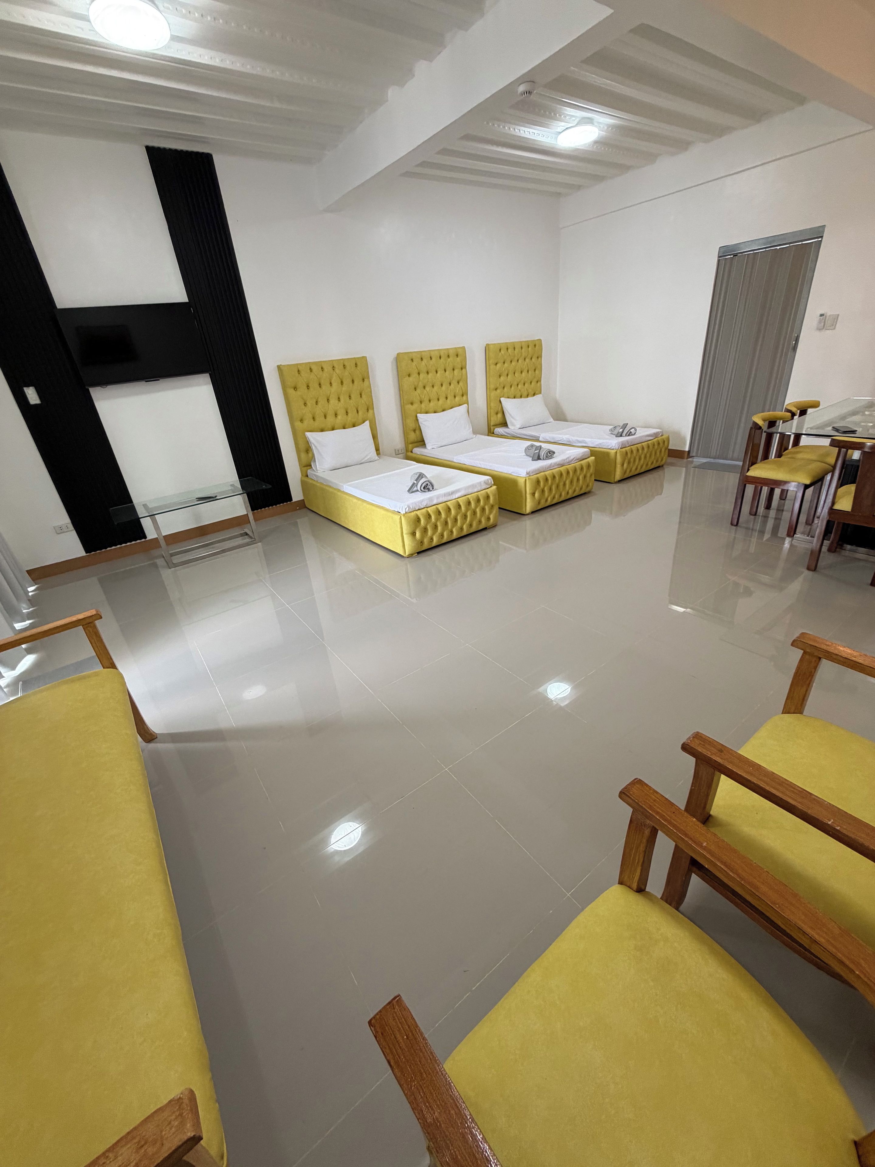 Habitación de hotel con tres camas, una mesa de vidrio y sillas de madera.