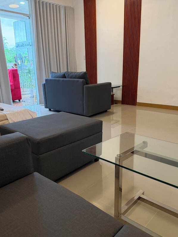 A modern living room with a grey sectional sofa, a glass coffee table, and a red chair outside.