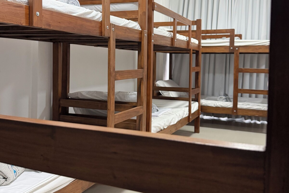 Habitación con literas de madera, una escalera y una cortina.