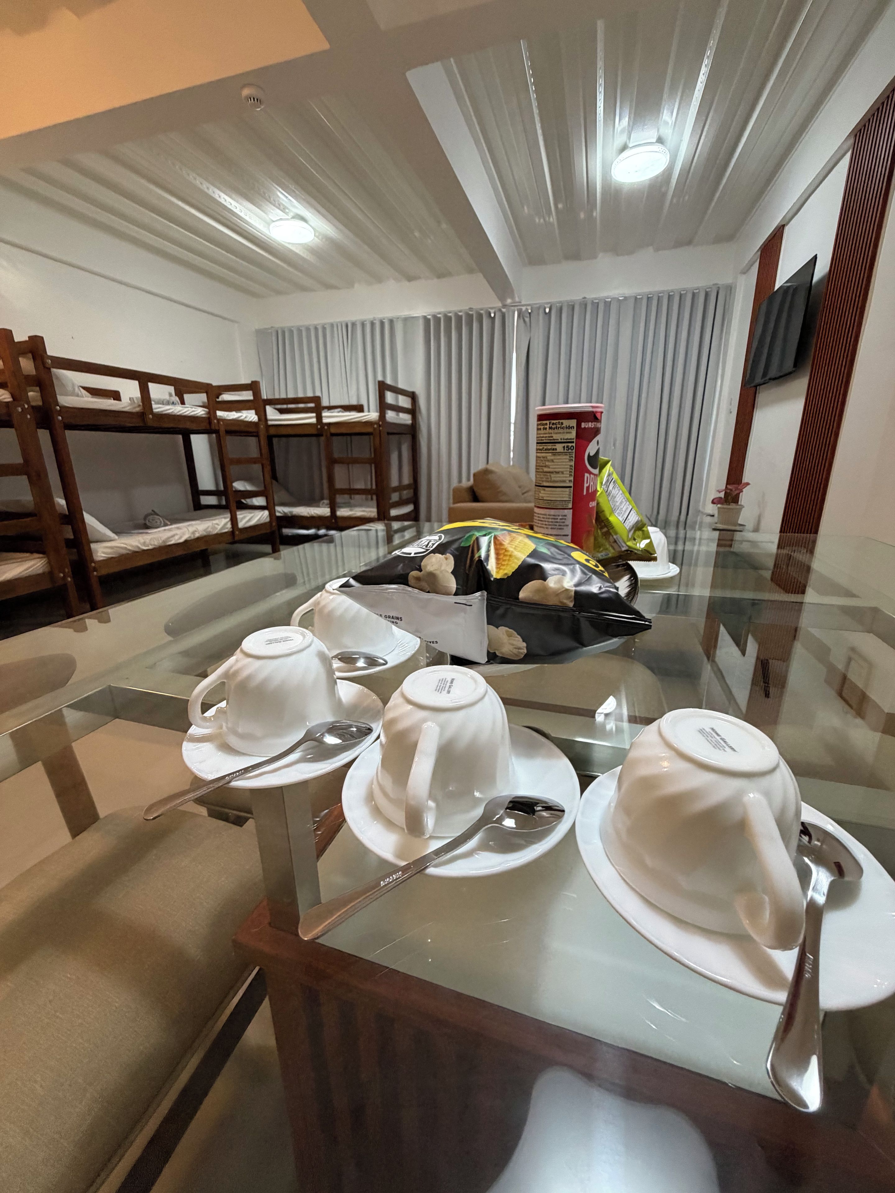 A room with bunk beds, a dining table with white teacups and saucers, and a bag of snacks.
