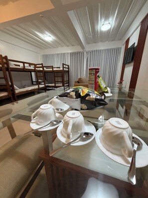 A room with bunk beds, a dining table with white teacups and saucers, and a bag of snacks.