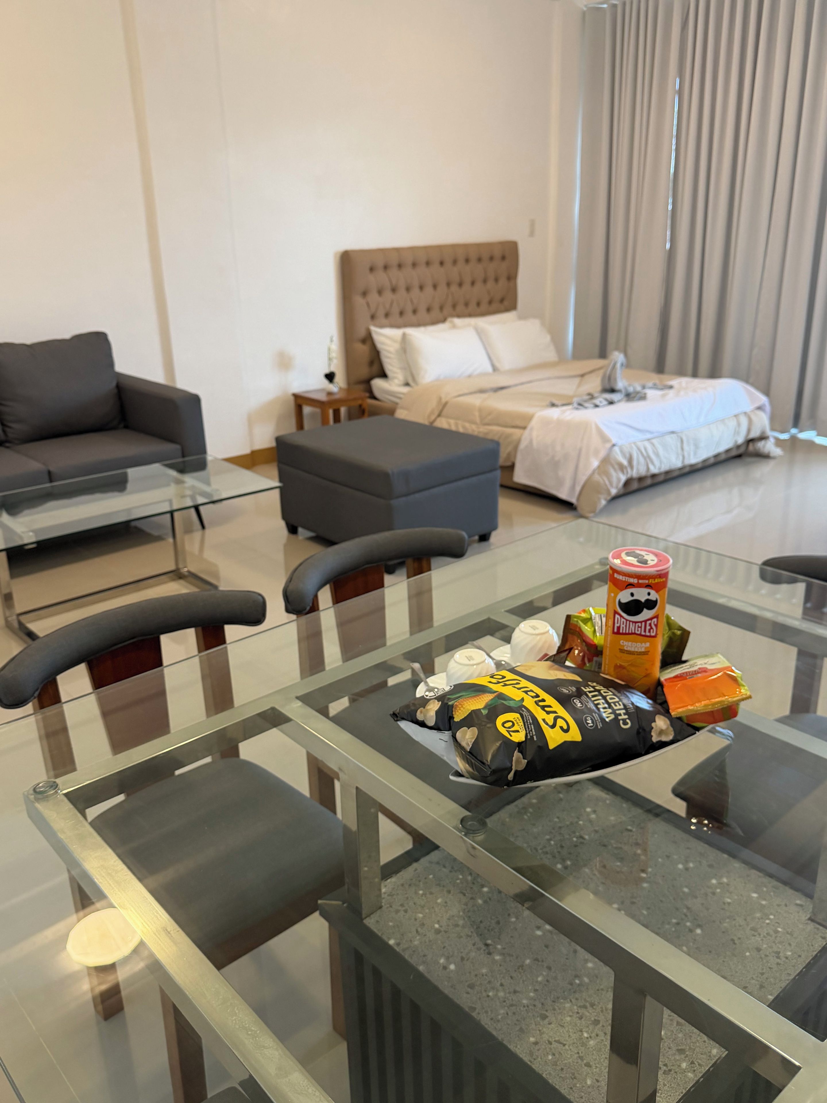 Una sala moderna con una mesa de centro de vidrio, un sofá, una cama con cabecera y un comedor con sillas.