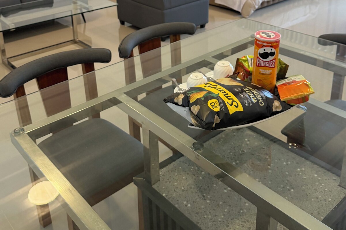 Un salon moderne avec une table basse en verre, un canapé, un lit avec une tête de lit et un coin repas avec des chaises.