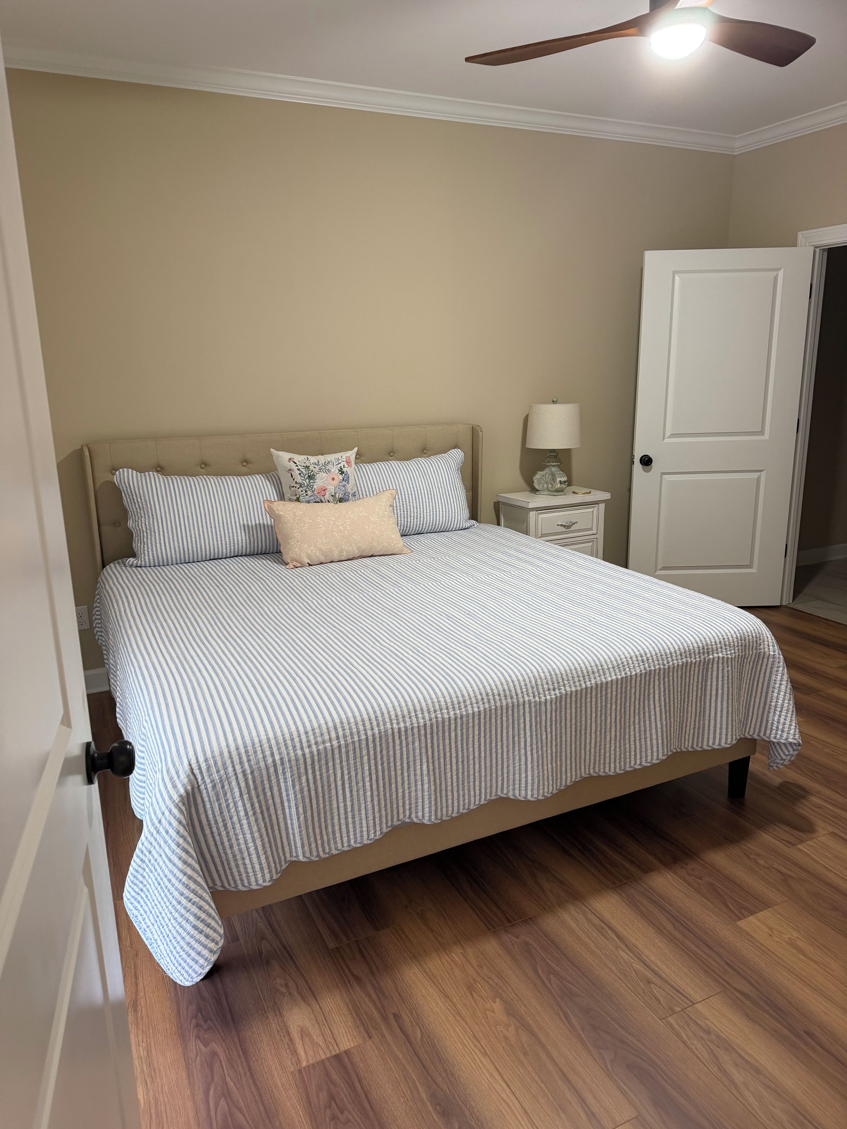 Un dormitorio con una cama, una mesita de noche, una lámpara y una puerta.