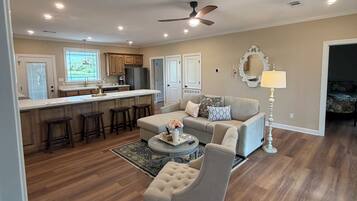 A spacious living area with a sofa, a coffee table, and a dining area with a kitchen in the background.