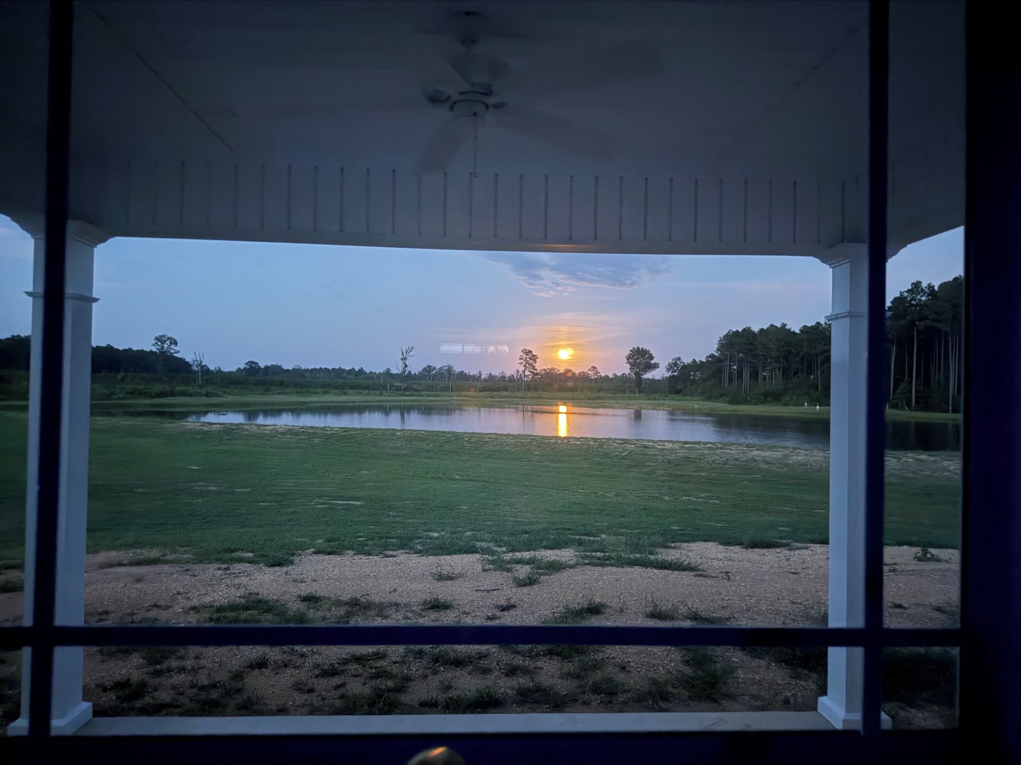 Vista desde un porche cubierto sobre un campo verde con un cuerpo de agua y árboles al fondo.