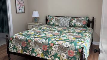 A bedroom with a wooden bed, a ceiling fan, a nightstand with a lamp, and a floral wall art piece.