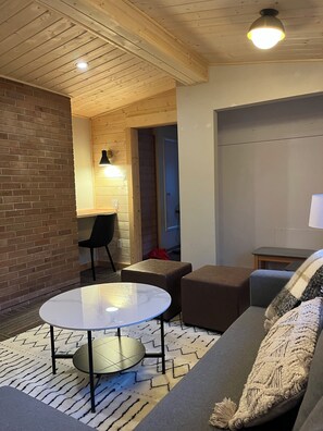 A cozy living area with a round table, two ottomans, a sofa, a lamp, and a brick wall. - Location, location! 5 minute walk to main street yet on a cute, quiet street! (Jasper)