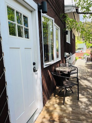 A wooden house with a white door and windows, a patio with a table and chairs, and a view of a backyard with a fence and a car. - Location, location! 5 minute walk to main street yet on a cute, quiet street! (Jasper)
