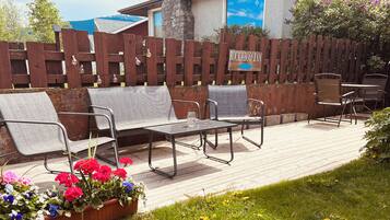 An outdoor seating area with metal chairs and a table, a wooden fence with a sign, and potted flowers.