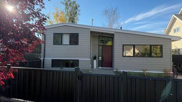 A modern two-story house with a dark brown gate, a red door, and a small porch area.