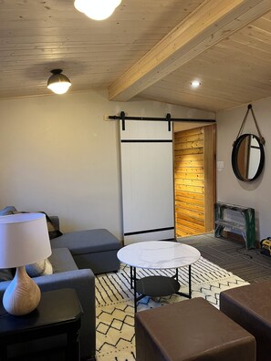 A modern living room with a sofa, a small round table, a lamp, and a hanging mirror. - Location, location! 5 minute walk to main street yet on a cute, quiet street! (Jasper)