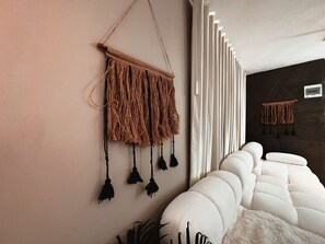 A modern living room with a white sofa, a wall-mounted macrame piece, and a dark accent wall. - Apartment Palace in Poblado (Medellín)