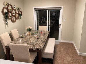 A dining area with a marble table, cushioned chairs, a bench, and a wall-mounted hexagonal shelf with various items. - The Cozy Grove | Family 3+1BR & Spacious Backyard (Kitchener)