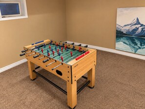 A foosball table in a room with a carpeted floor and a painting on the wall. - The Cozy Grove | Family 3+1BR & Spacious Backyard (Kitchener)