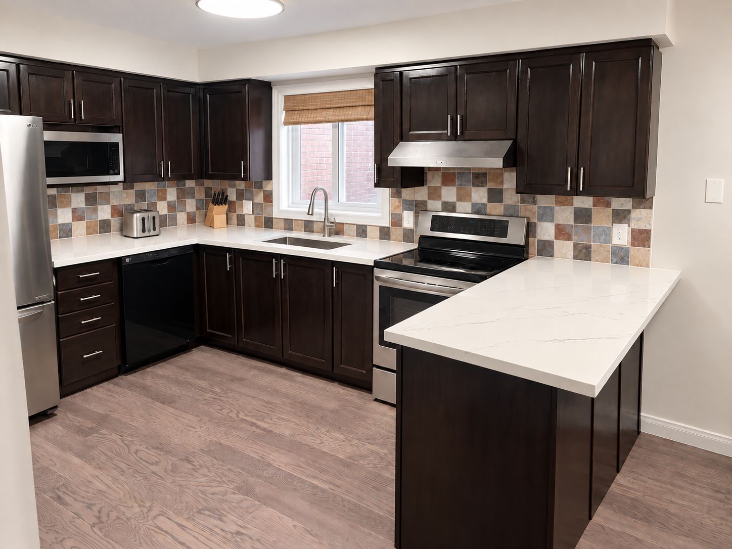 A modern kitchen with dark wood cabinets, a stainless steel microwave, a built-in oven, and a large island with a white countertop.
