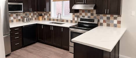 A modern kitchen with dark wood cabinets, a stainless steel microwave, a built-in oven, and a large island with a white countertop.