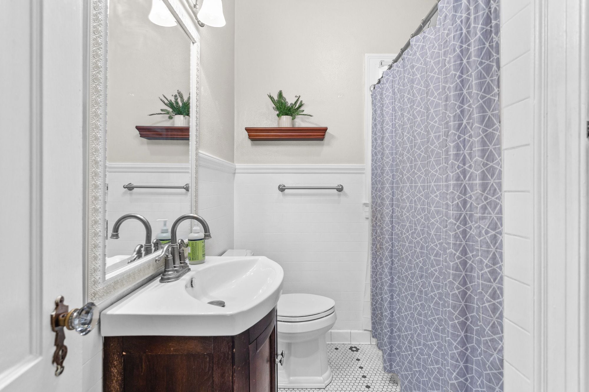 Een badkamer met een witte wastafel, toilet en een douchegordijn met een geometrisch patroon.
