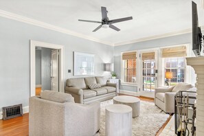 A living room with a ceiling fan, two sofas, a coffee table, and a view through large windows. - Downtown 3-bedroom HPU & Furniture Mkt (High Point)