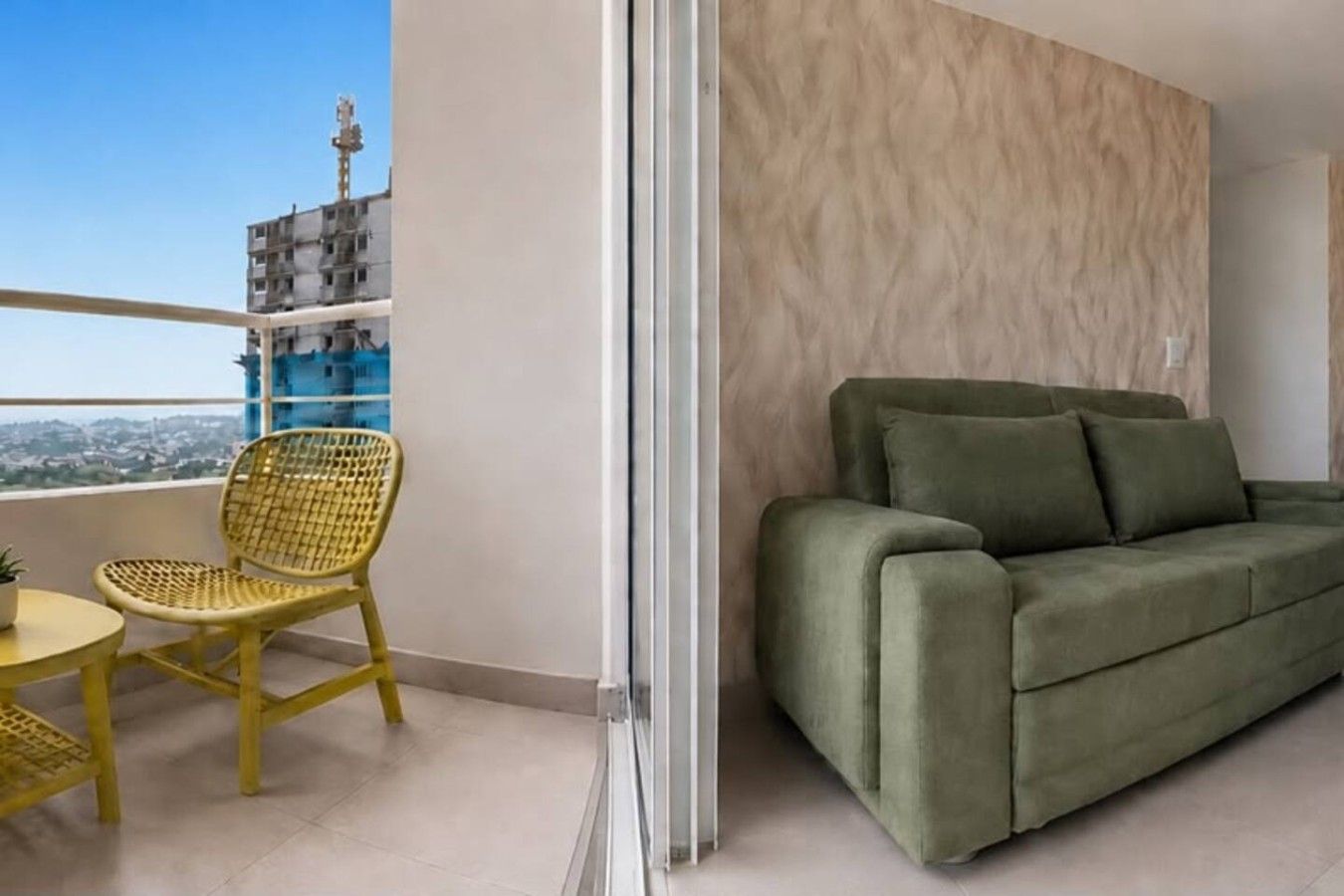 Un balcon avec une chaise jaune et une petite table, un canapé vert et une vue sur un immeuble.