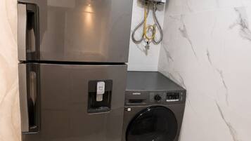 A compact kitchen with a stainless steel refrigerator and a washing machine.