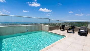 A rooftop swimming pool with clear blue water, surrounded by a glass railing, and overlooking a cityscape.