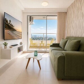 A modern living room with a green sofa, a flat-screen TV, a small table with a vase, and a balcony with yellow chairs. - Citrus Cove | Sea Views, Pool & 3BR (Cartagena)