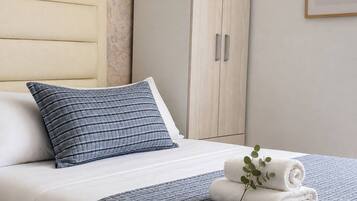A neatly made bed with a striped blanket and pillows, a wooden wardrobe, and a framed plant on the wall.