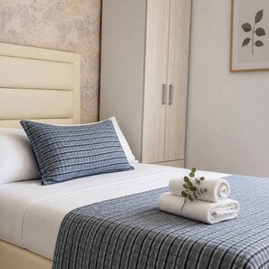A neatly made bed with a striped blanket and pillows, a wooden wardrobe, and a framed plant on the wall. - Citrus Cove | Sea Views, Pool & 3BR (Cartagena)