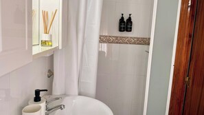 Un baño con un lavamanos blanco, un espejo, una cortina de ducha y dos botellas de champú y gel de baño en la pared.