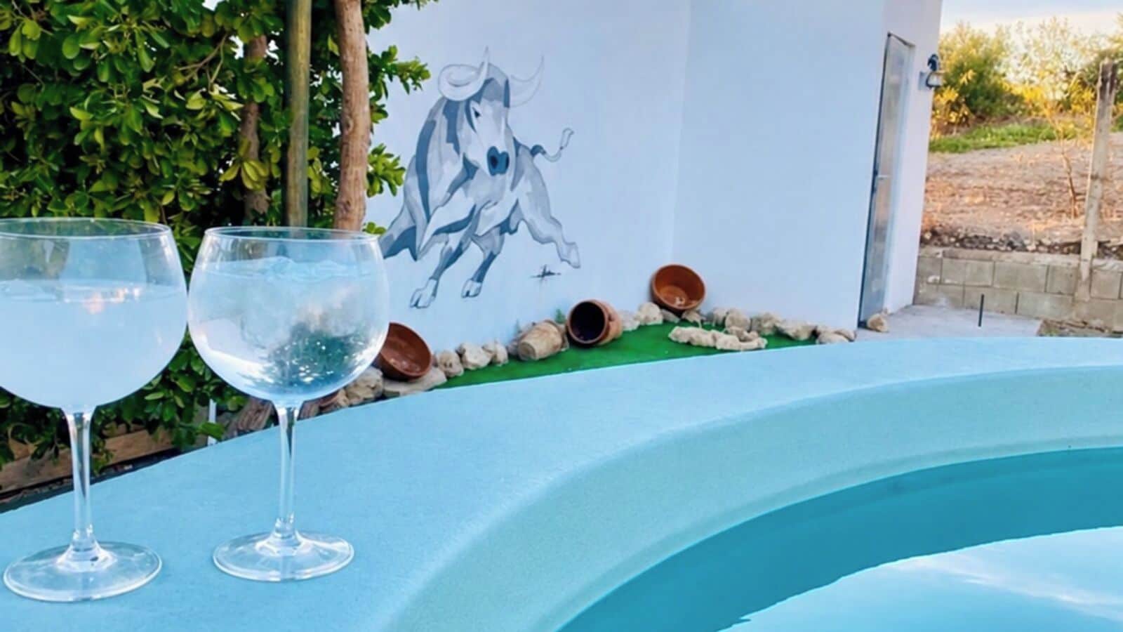 A swimming pool with two clear glasses on the edge, a mural of a horse, and a stone wall in the background.